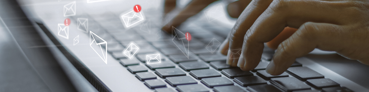 Közelkép egy személy kezéről, ahogy laptopon gépel, körülötte lebegő e-mail ikonokkal.