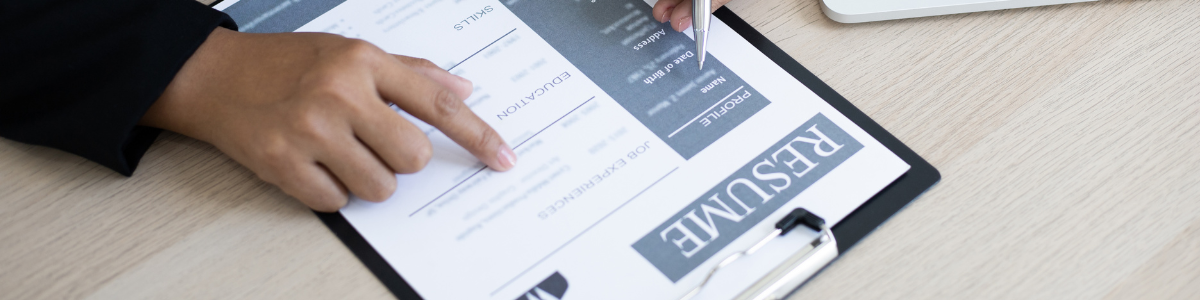 Közelkép egy kézről, amely egy önéletrajzra mutat egy írótáblán.